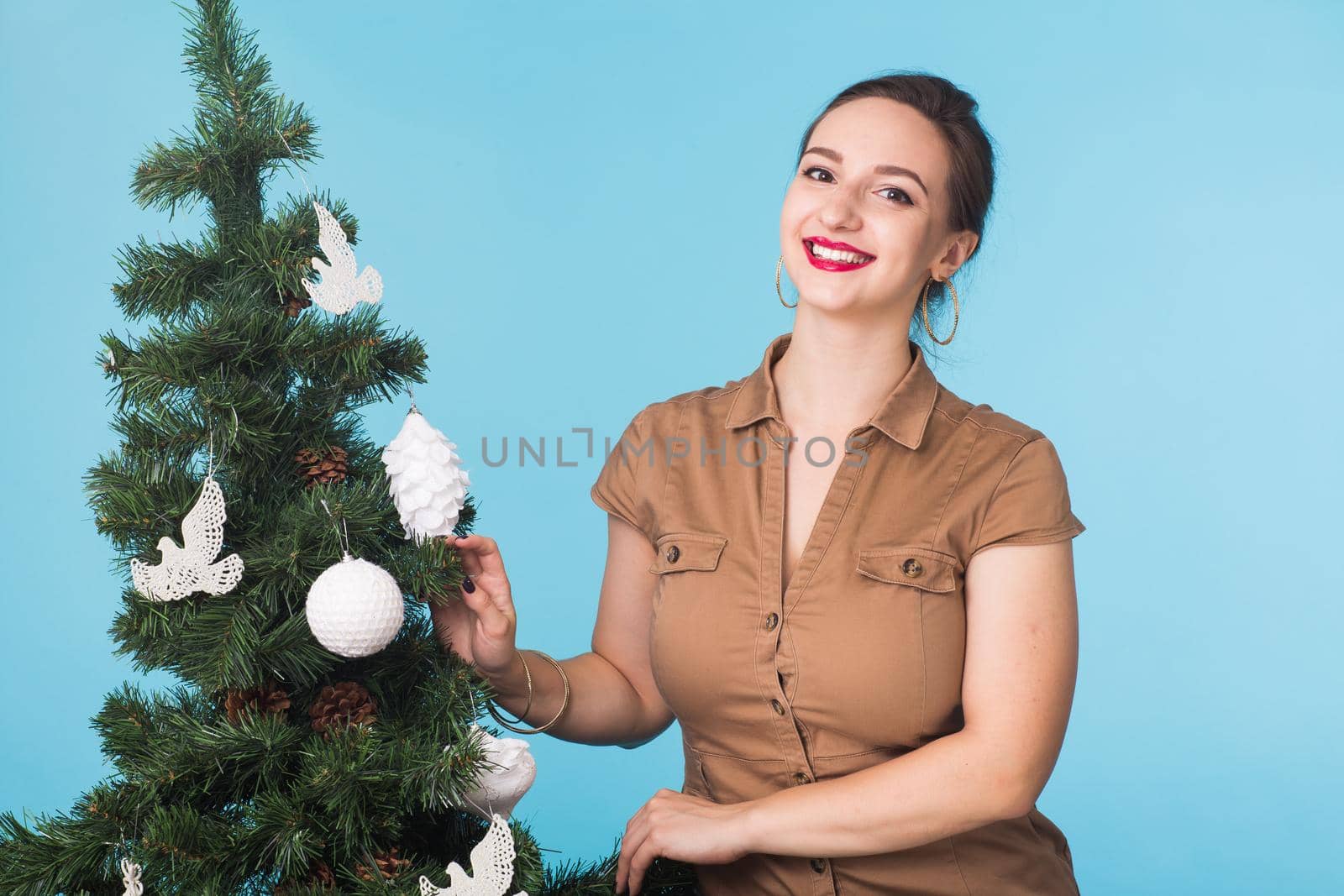 People and holidays concept - Portrait of smiling young woman with Christmas tree on blue background by Satura86