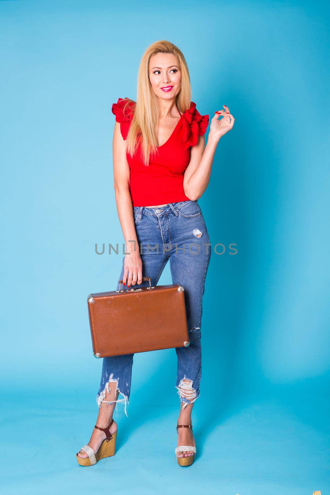 Portrait of a beautiful young blonde woman with retro suitcase on blue background