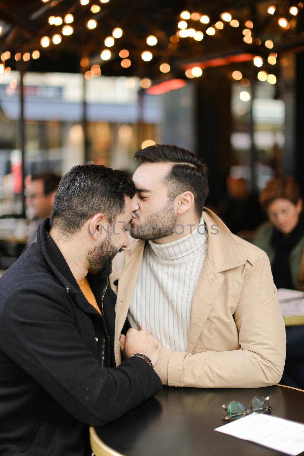 Caucasian gays sitting at street cafe, kissing and hugging. Concept of relationship and same sex couple.