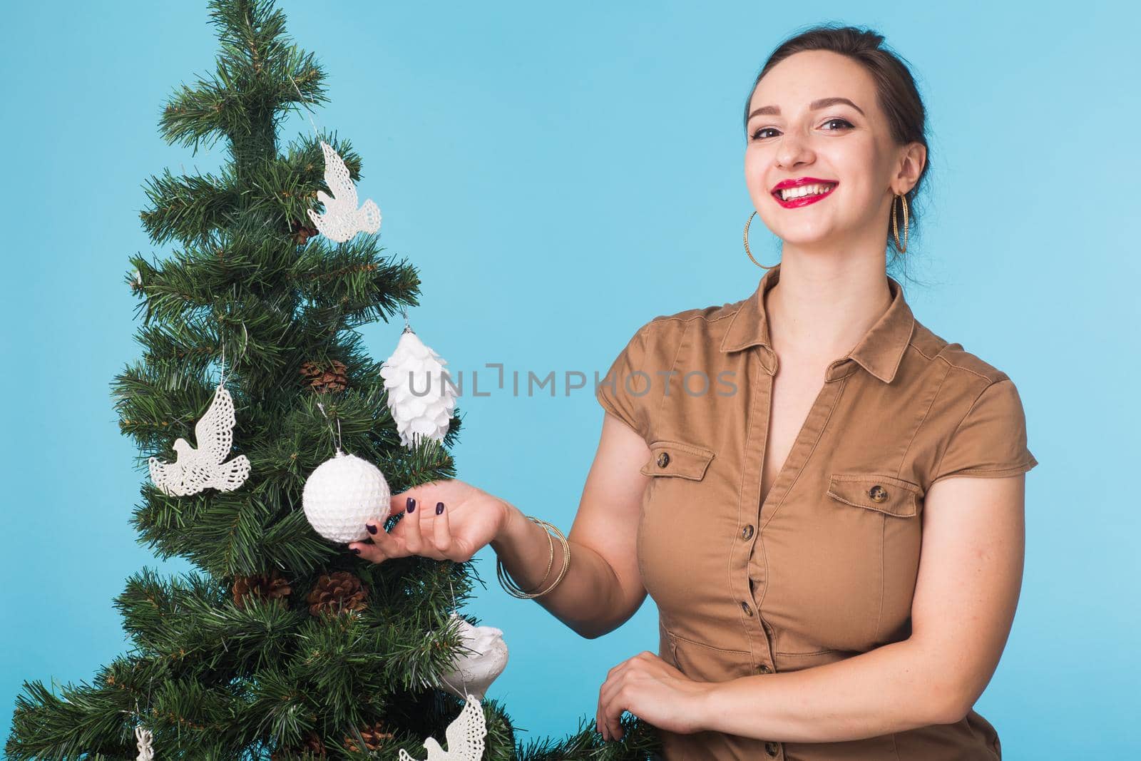 People and holidays concept - Portrait of smiling young woman with Christmas tree on blue background