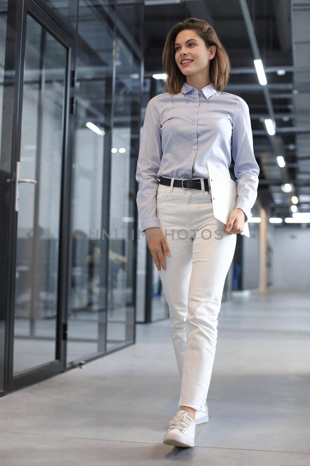 Businesswoman walking along the office corridor with documents