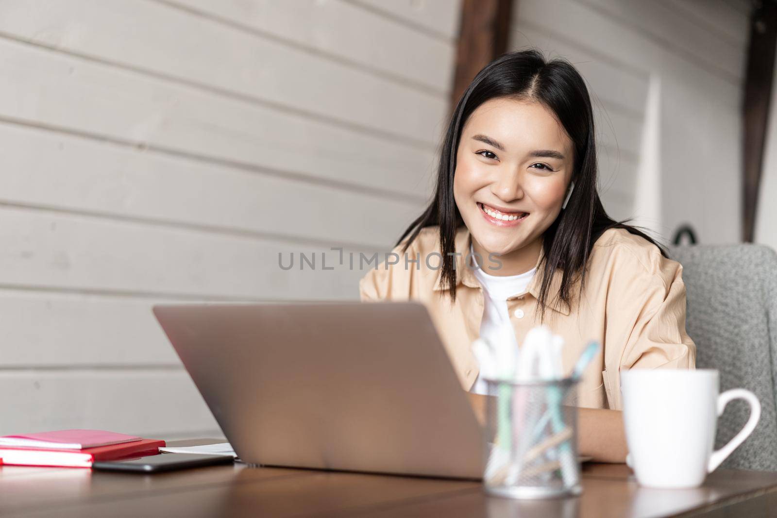 Smiling korean girl works from home, woman freelancer working on laptop, studying or doing homework on computer.