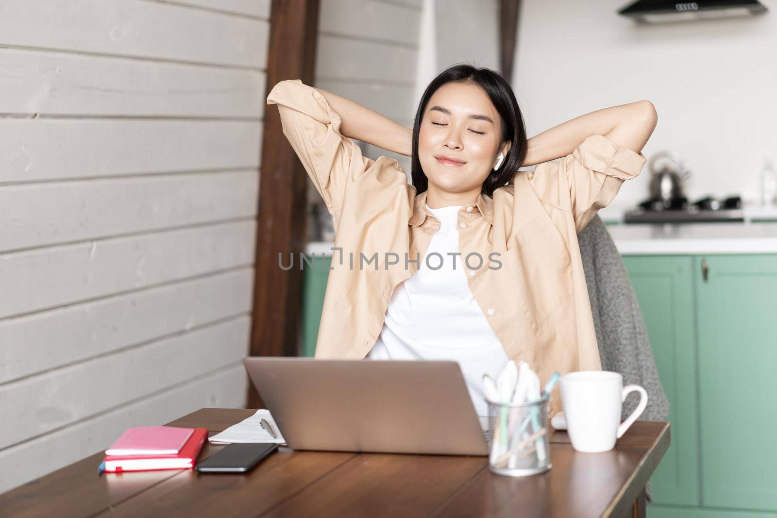 Work from home and distance education concept. Young asian girl finished online course, stretching and lay back on chair, resting from laptop by Benzoix