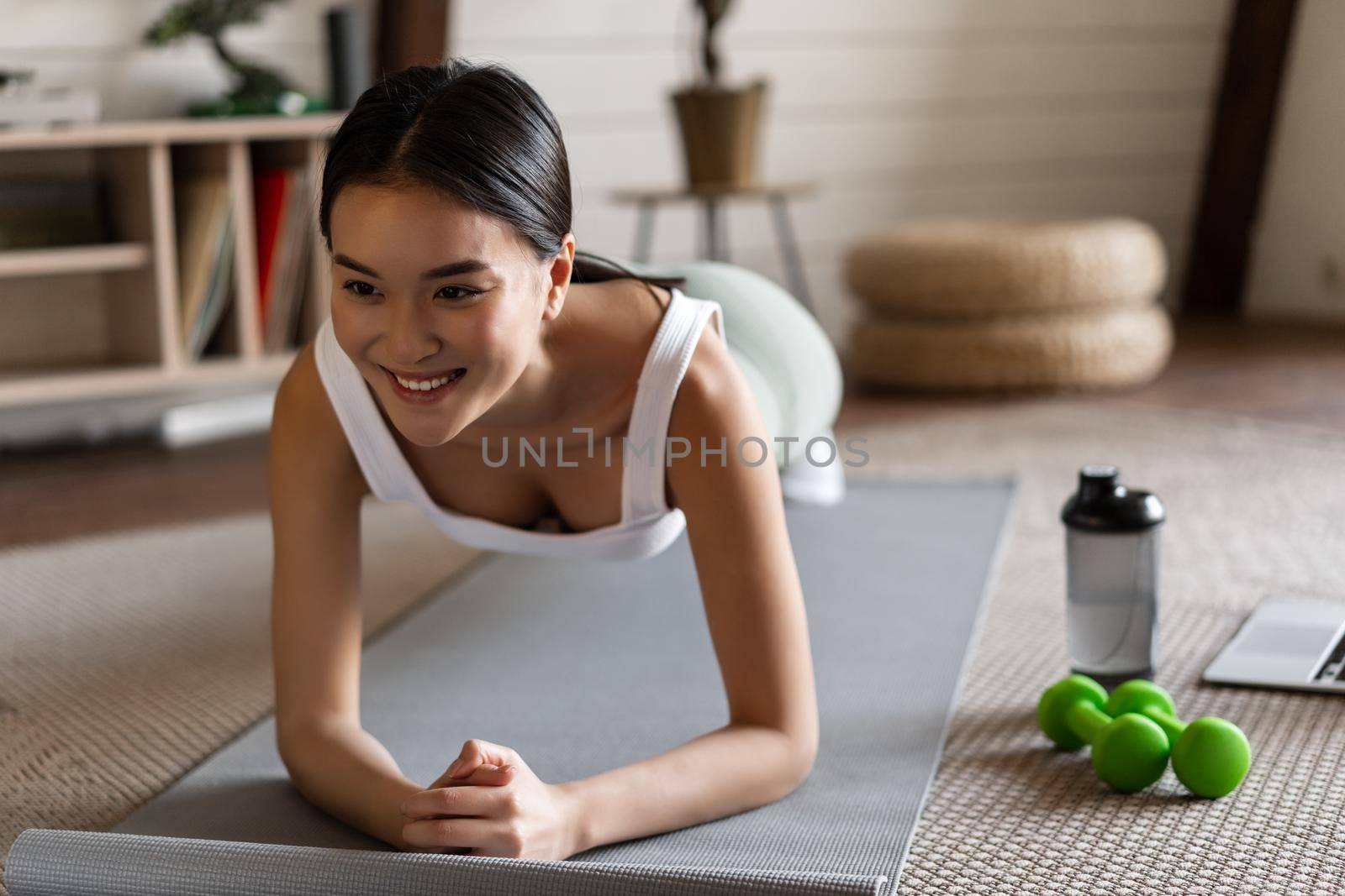 Sporty asian girl in activewear doing workout at home, follow video sport guide, online fitness instructor on laptop, standing in plank on floor mat by Benzoix