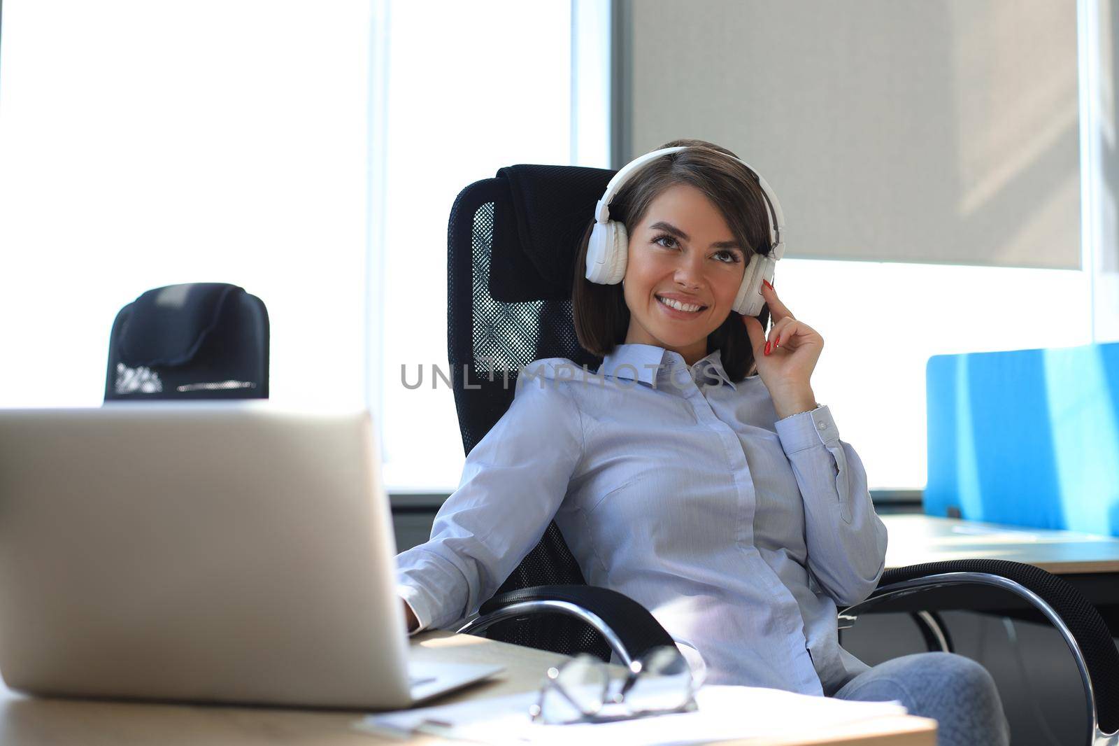 Young woman having a break and listening music in headphones sitting on working place