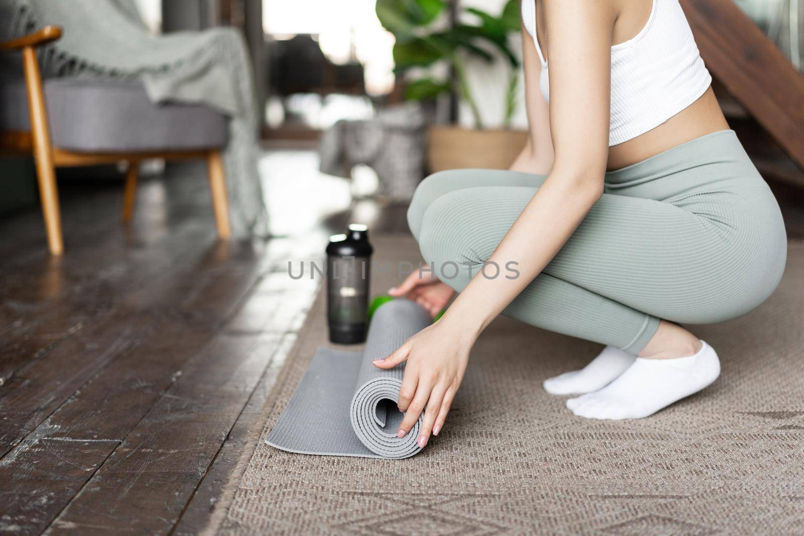 Cropped shot of woman rolling out floor mat for yoga, fitness training at home, girl prepare place for workout at home.