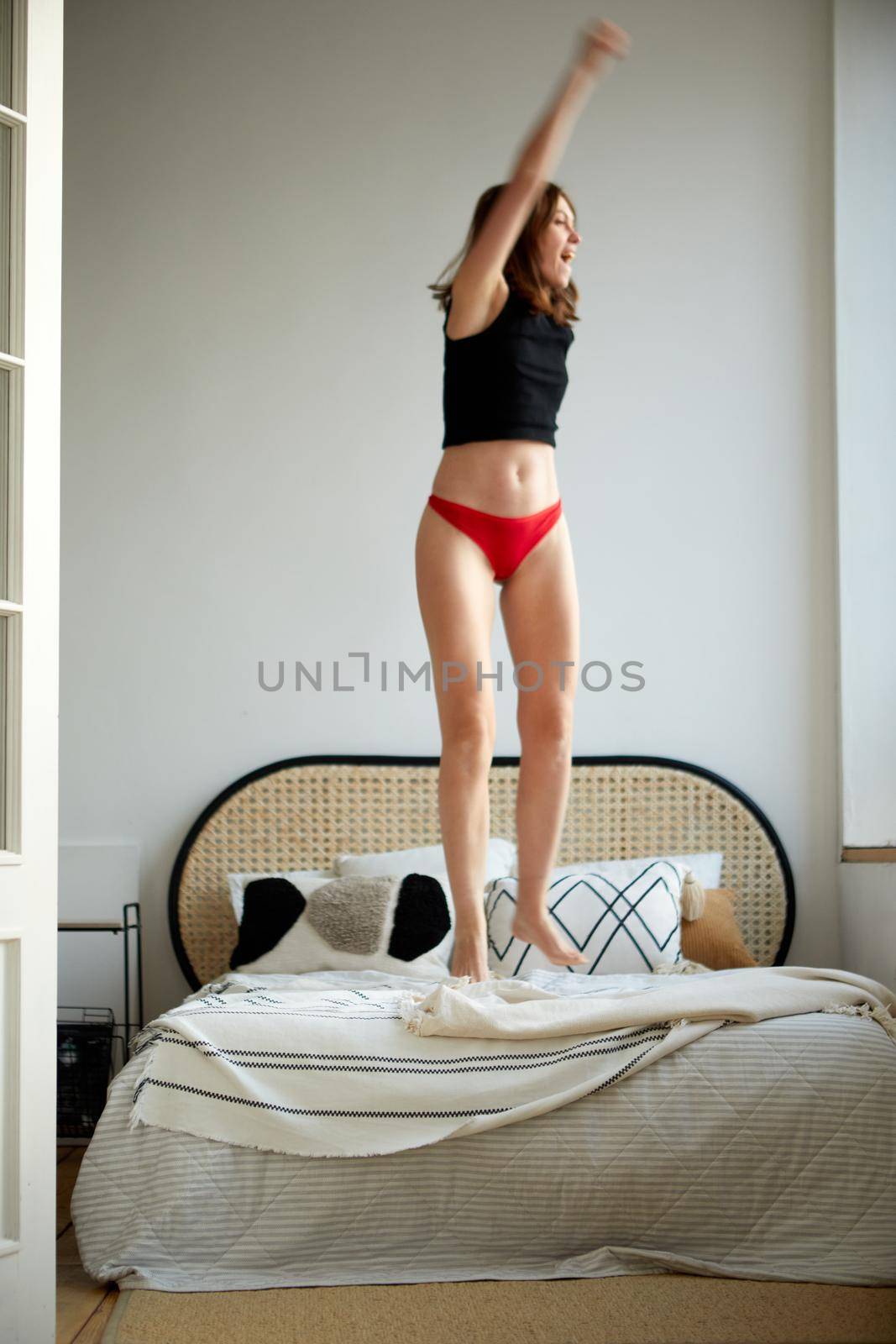 Cheerful woman jumping on bed at home by Demkat