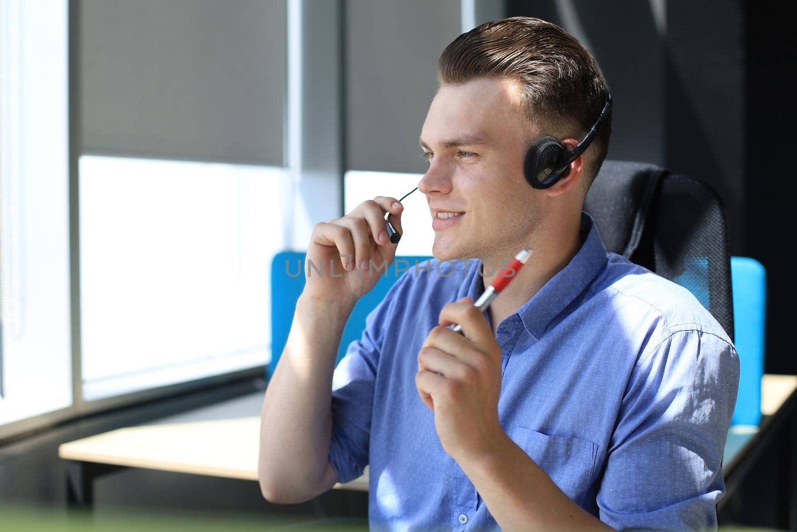 Cheerful young support phone male operator in headset, at workplace while using laptop, help service and client consulting call center concept.