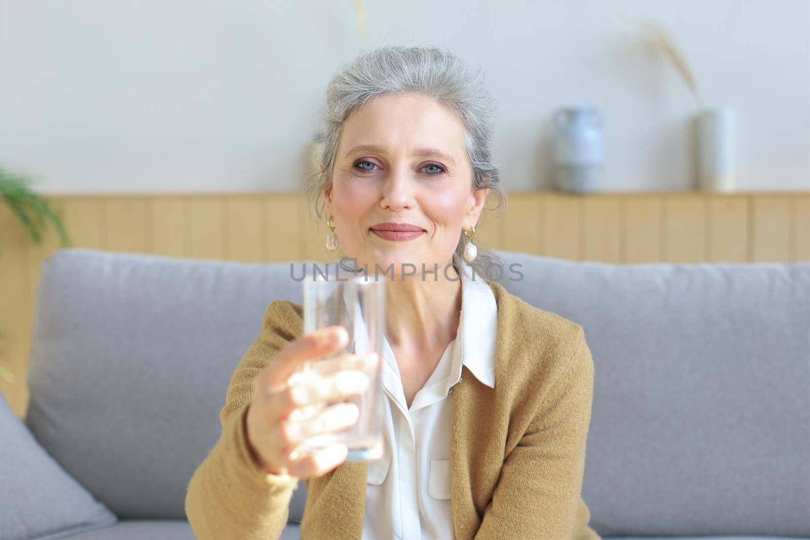 Attractive middle aged woman holding glass of water and looking at camera. Healthy lifestyle