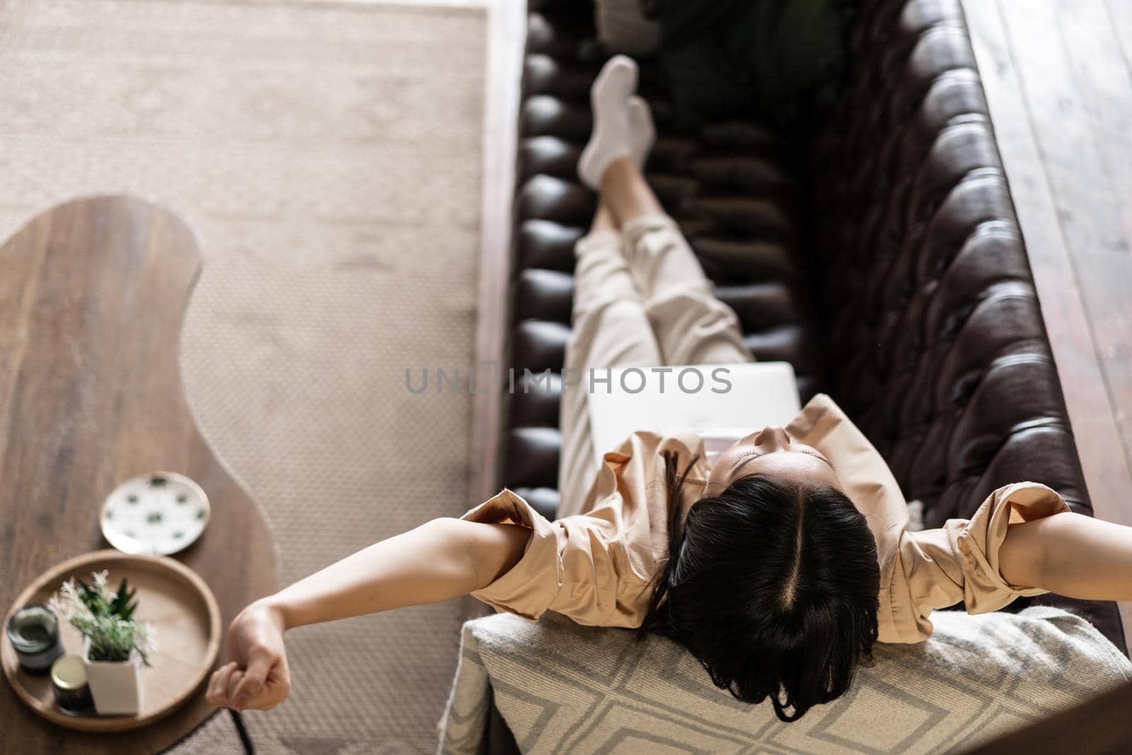 Young woman laying on couch with laptop and doing victory stretch, resting at home on weekday.
