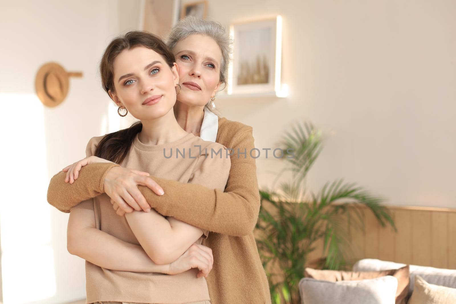 Beautiful mother and daughter. Cheerful young woman is embracing her middle aged mother in living room. Family portrait