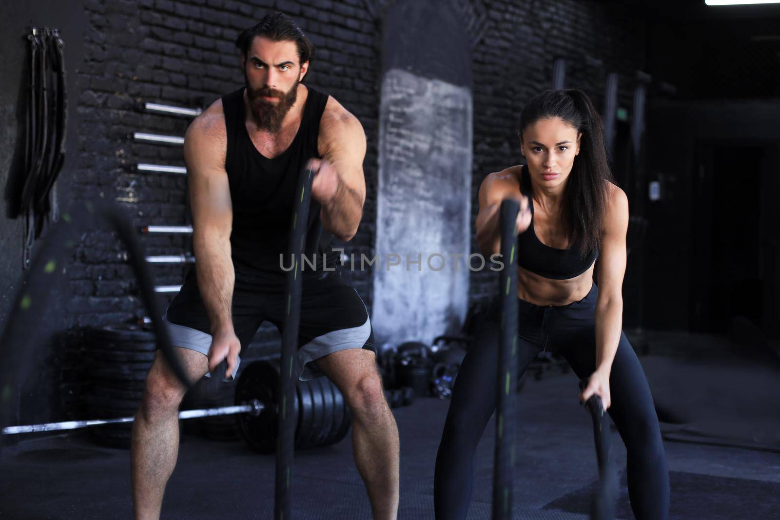 Athletic young couple with battle rope doing exercise in functional training fitness gym