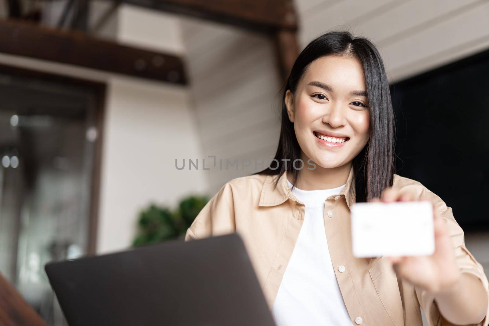 Online shopping. Young woman paying for purchase with credit card, buying on websites on laptop, sitting at home in living room.