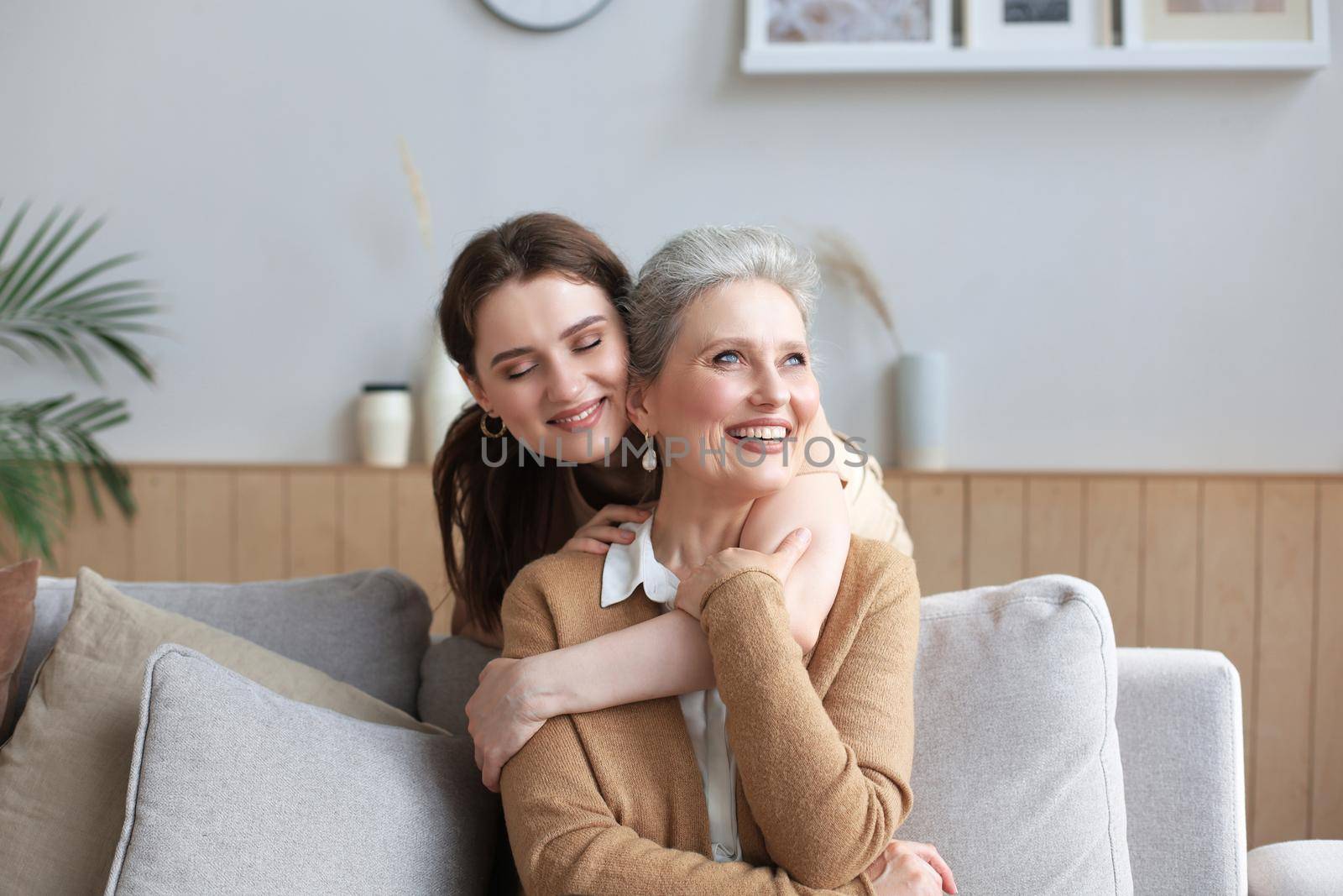 Portrait of old mother and mature daughter hugging at home. Happy senior mom and adult daughter embracing with love on sofa
