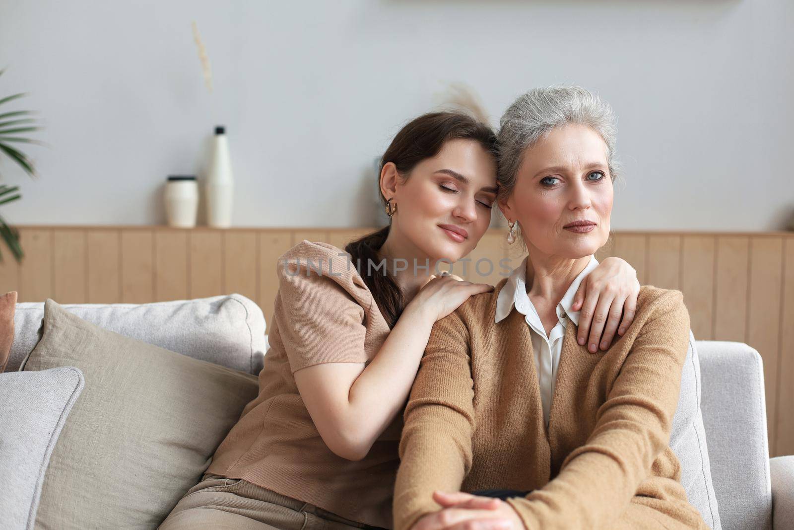 Portrait of old mother and mature daughter hugging at home. Happy senior mom and adult daughter embracing with love on sofa