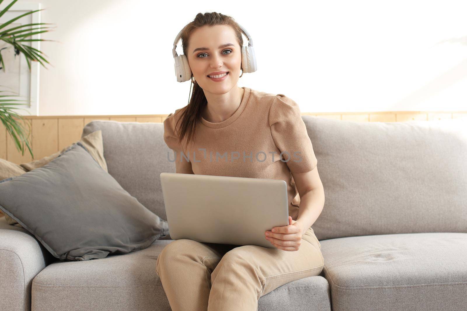 Smiling young woman with headphones and laptop on the sofa