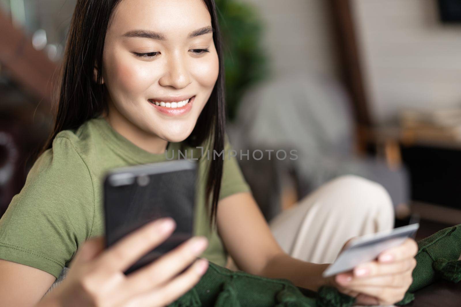 Young asian woman buying from online shop, using mobile phone and credit card, shopping from home.