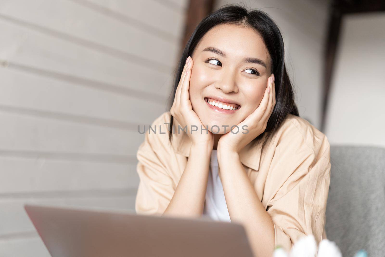 Asian woman smiling while resting, using laptop, watching videos or surfing net on computer, working from home.