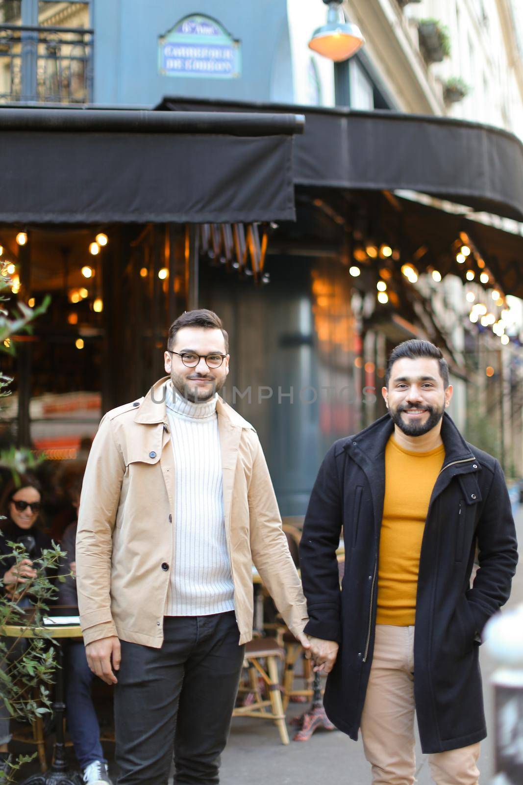 Two european gays standing at street cafe and holding hands. Concept of same sex couple and male friendship.