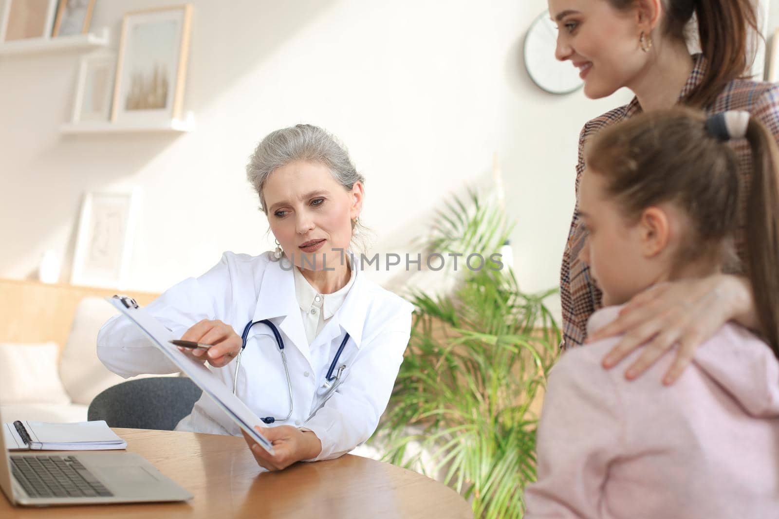 Mother and child in the doctor office meeting the pediatrician, they are sitting at desk in hospital