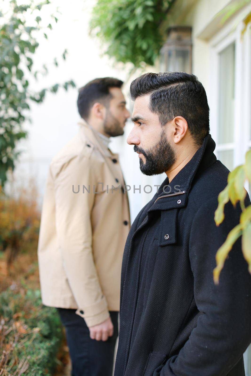 Focus on fisrt caucasian brunette man standing near boy and house. Concept of male person and two brothers.