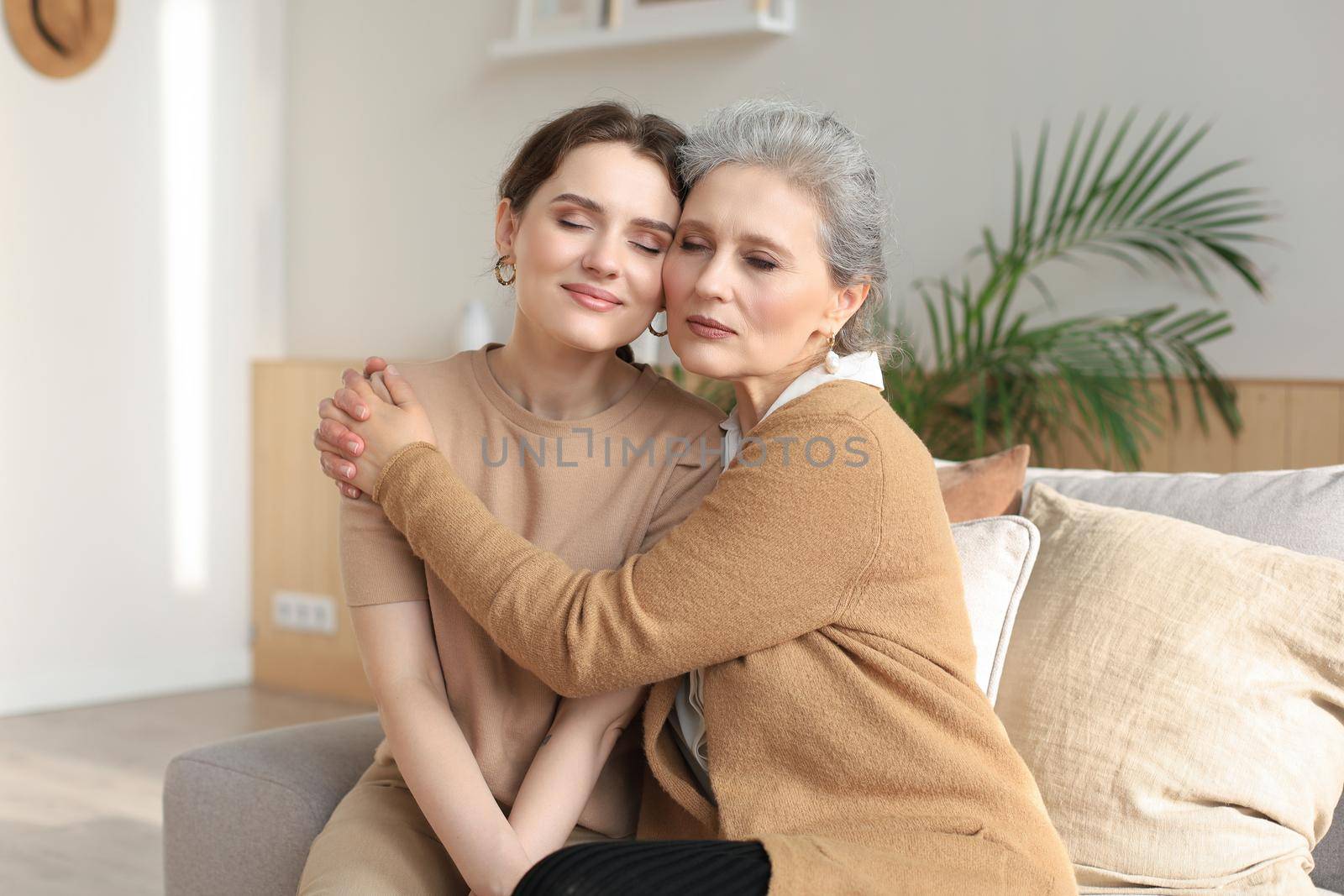Portrait of old mother and mature daughter hugging at home. Happy senior mom and adult daughter embracing with love on sofa
