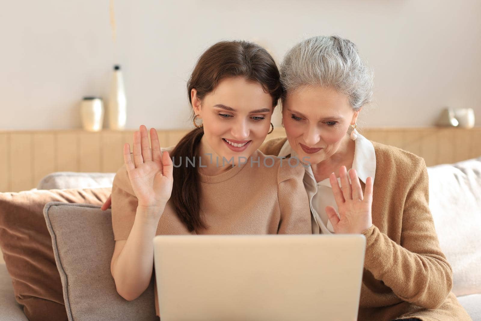 Happy elderly middle mother sitting on couch with her daughter, looking at laptop. Young woman showing video, photos to mommy, trusted relations. Family concept