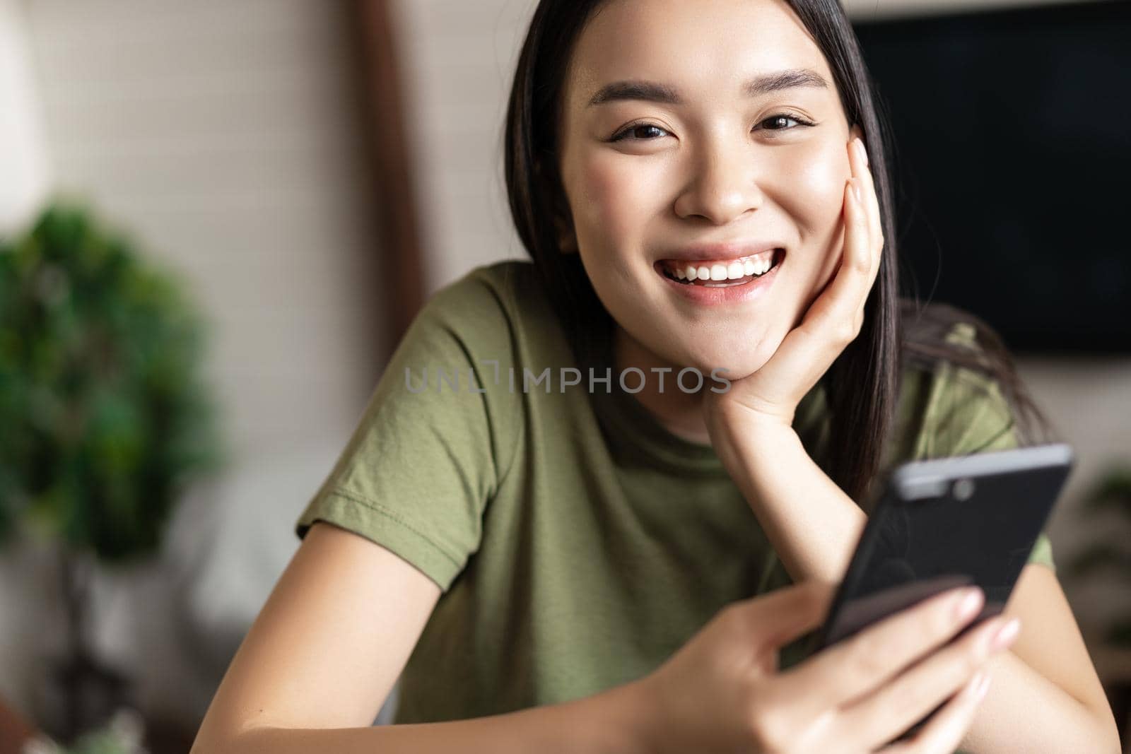 Smiling asian woman using mobile phone from home, making order, deliver smth to her house.