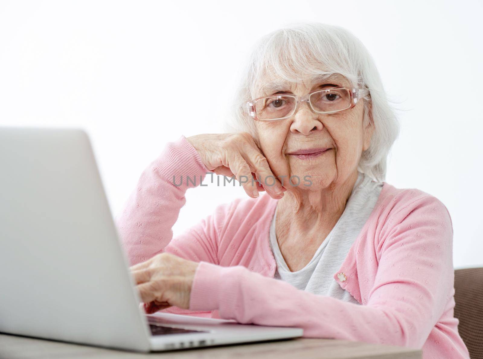 Senior woman with laptop sitting at home and looking at the camera. Portrait of elderly person with modern technologies