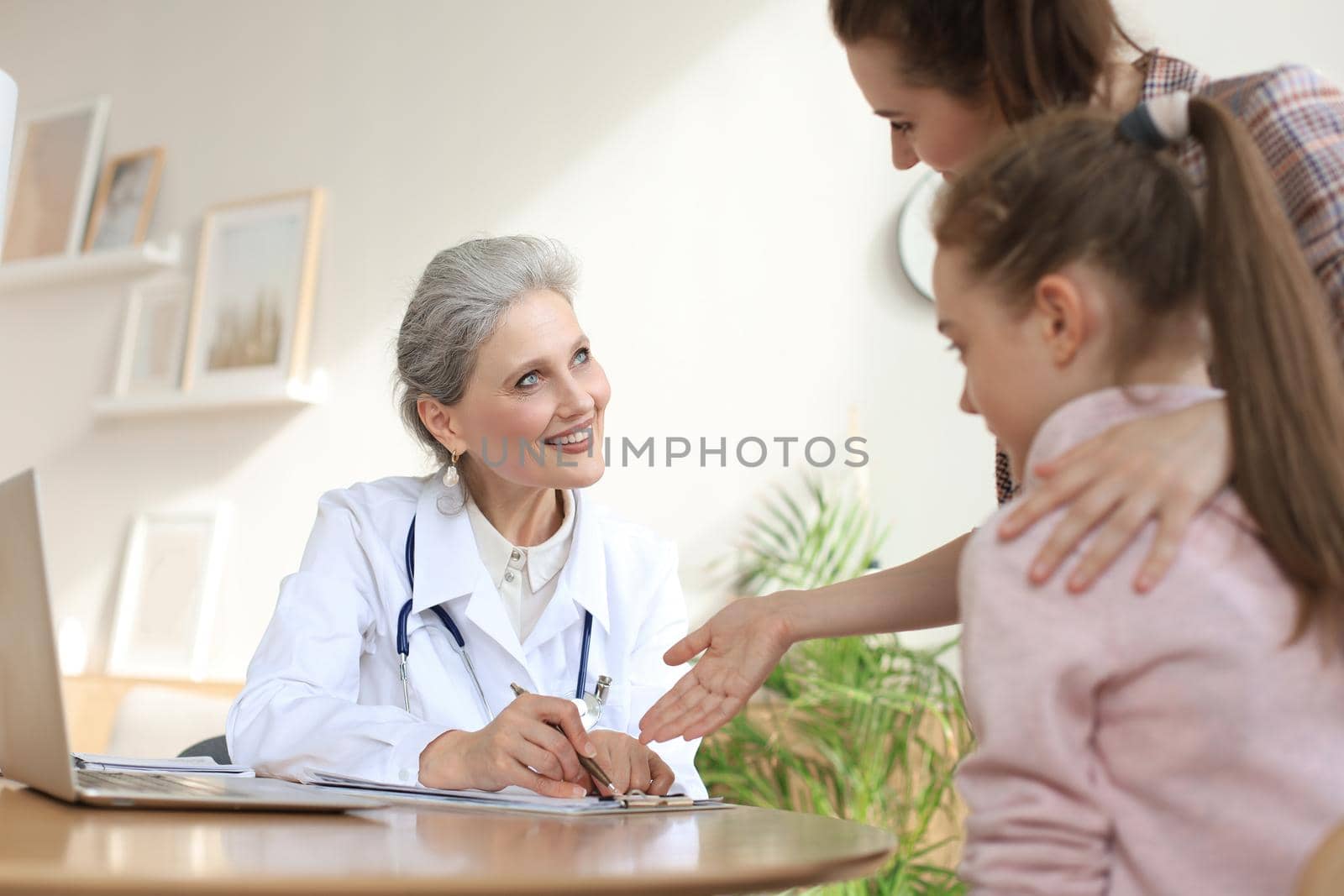 Mother and child in the doctor office meeting the pediatrician, they are sitting at desk in hospital