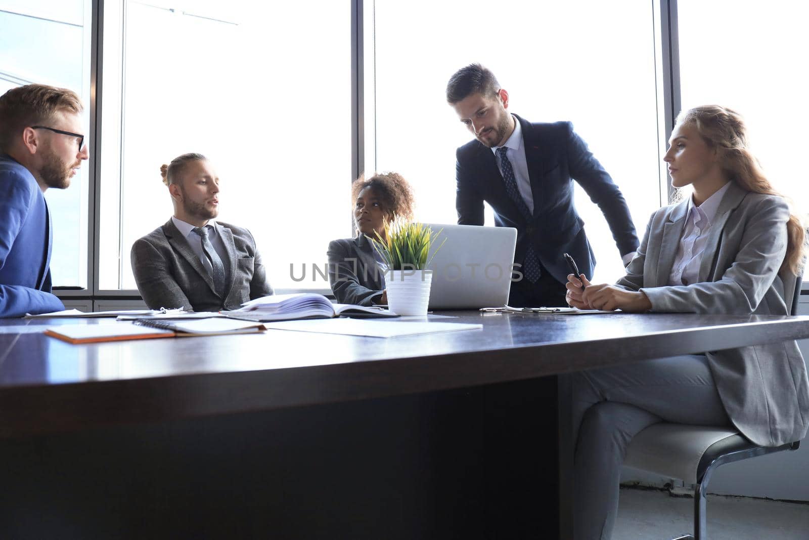 Group of modern business people in formalwear discussing business and smiling while sitting in the office.