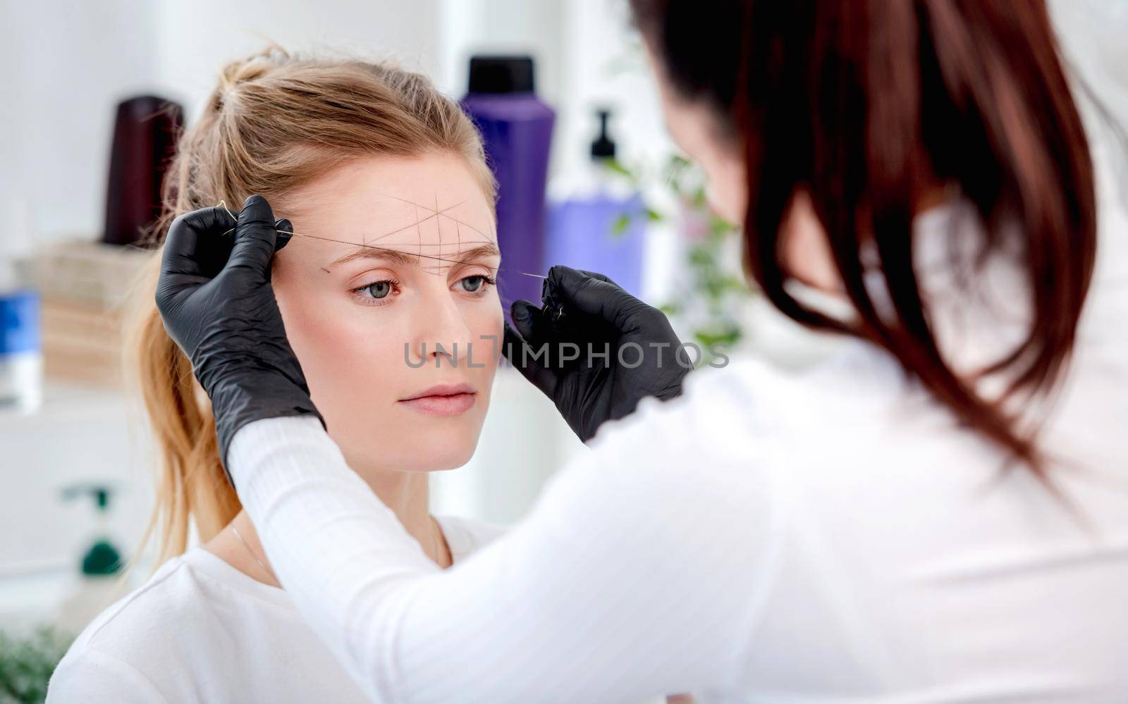 Master preparing for permanent makeup and shaping eyebrows with professional tools