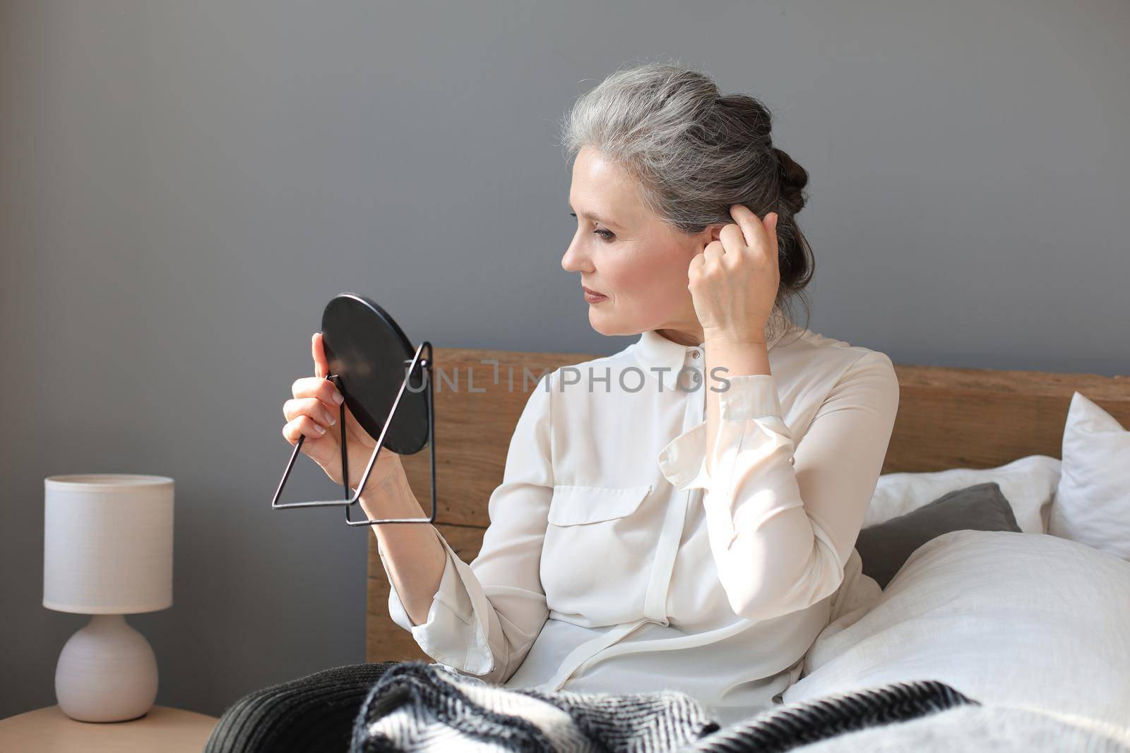 mature woman looking at mirror and touching face at home