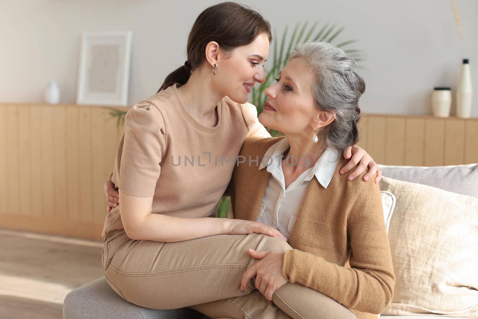 Portrait of old mother and mature daughter hugging at home. Happy senior mom and adult daughter embracing with love on sofa