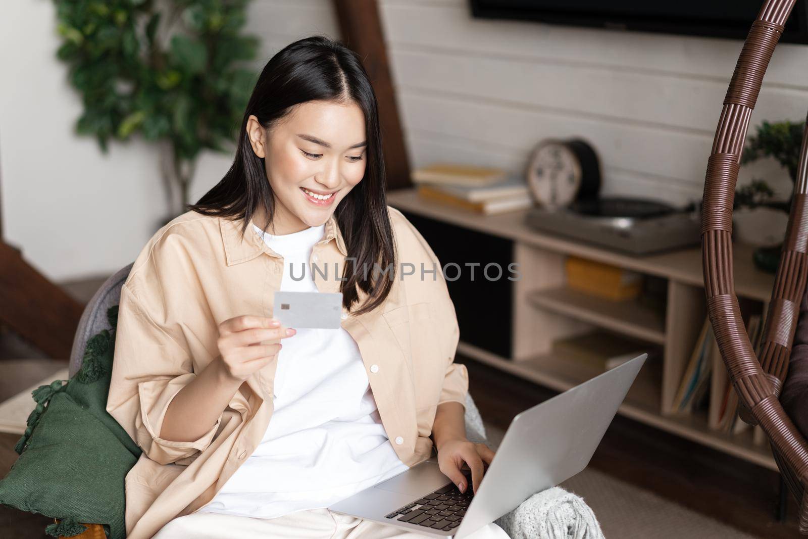 Smiling korean girl buying online from home, shopping on laptop and holding credit card.