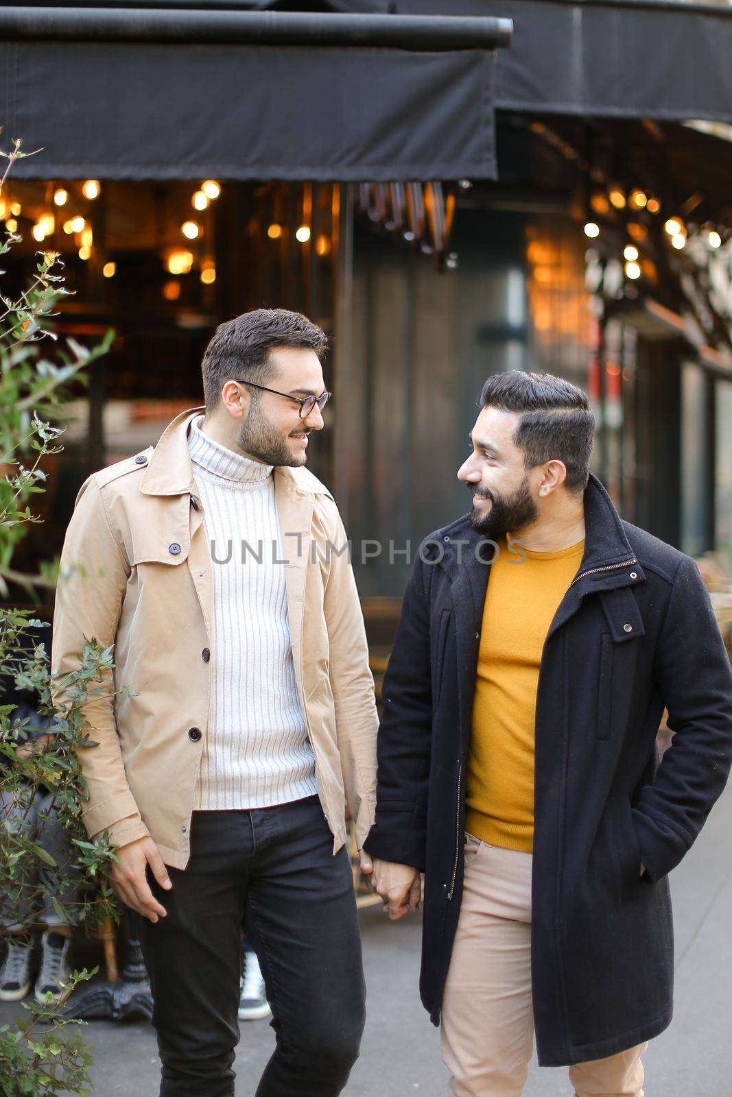 Two young caucasian gays standing at street cafe and holding hands. Concept of same sex couple and male friendship.