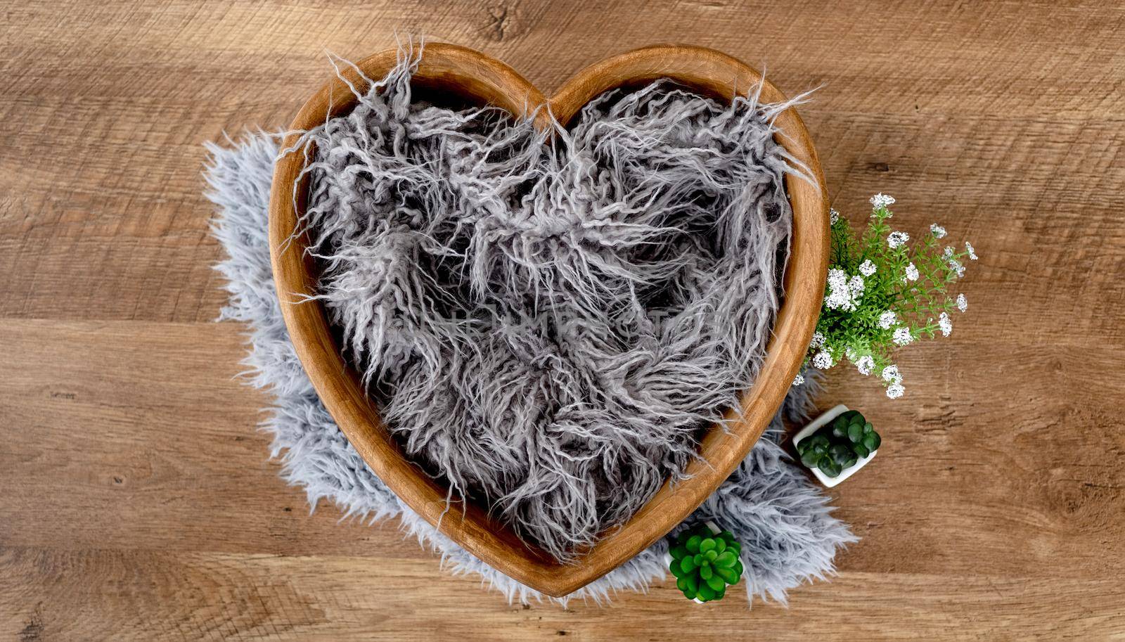 Decoration for newborn studio photoshoot. Tiny wooden shape heart bed with fur and flowers for infant baby photos