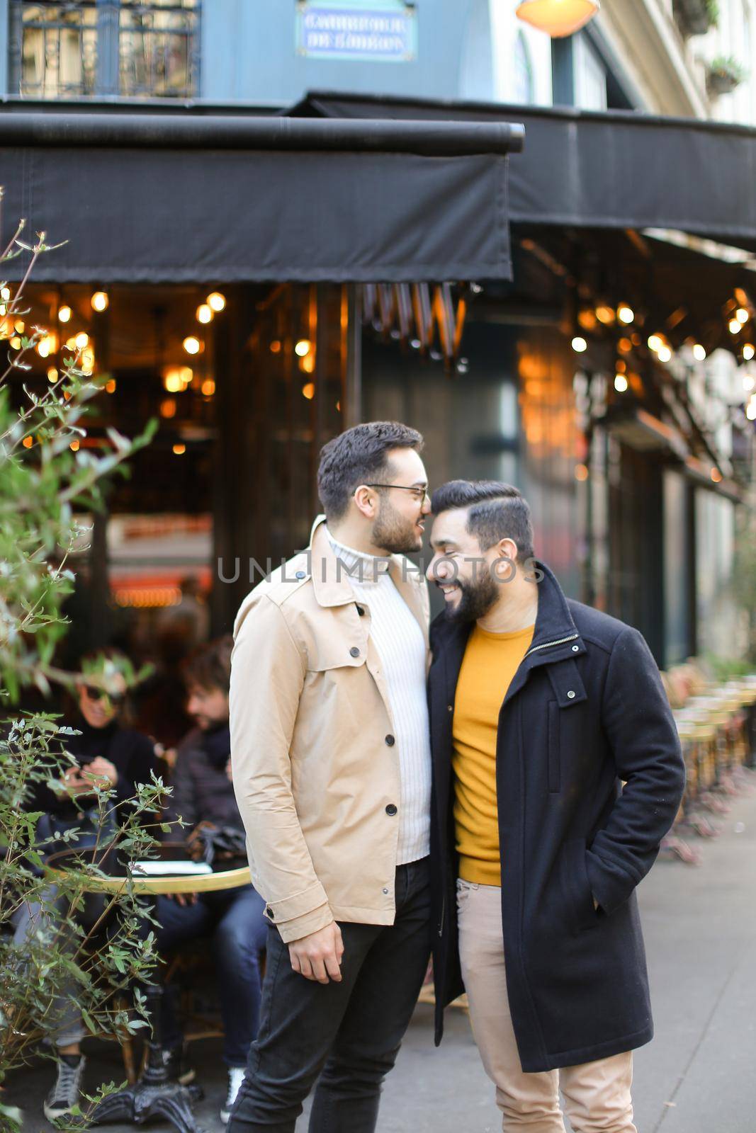 Two young gays standing at street cafe and smiling. Concept of same sex couple and male friendship.