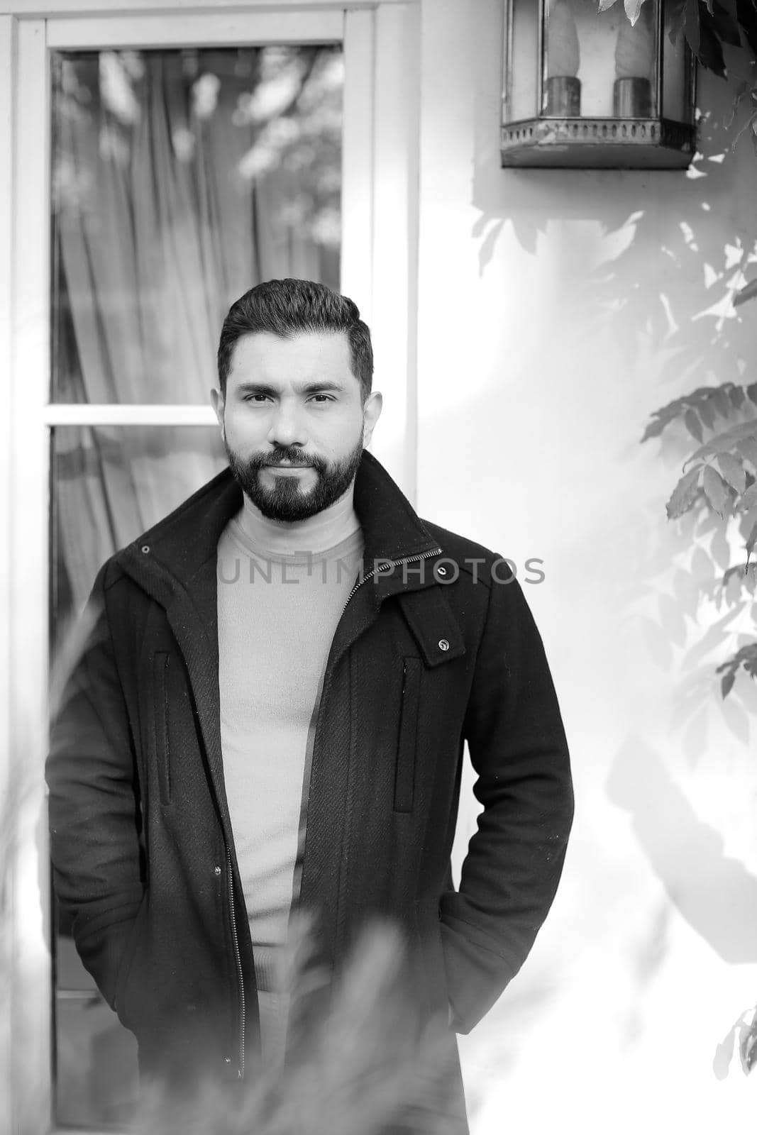 Black and white photo brunette handsome man standing near window. Concept of male person.