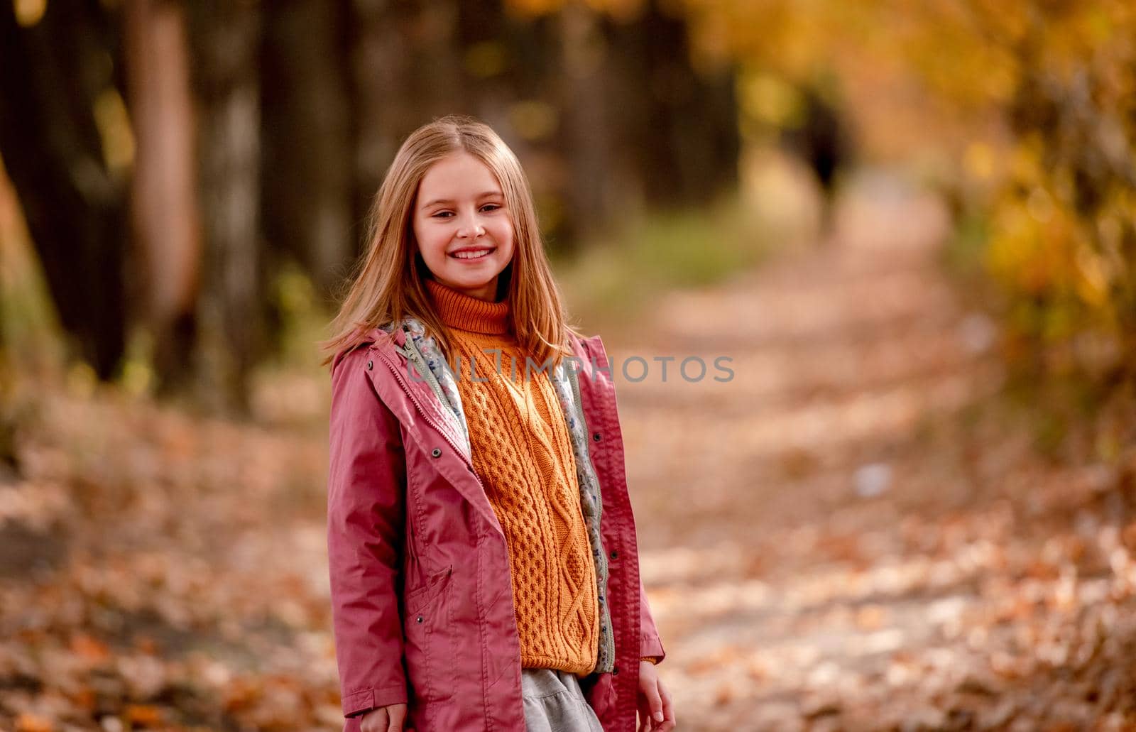 Beautiful girl kid looking at camera and smiling at nature with blurred yellow leaves on background. Cute child schoolgirl at park