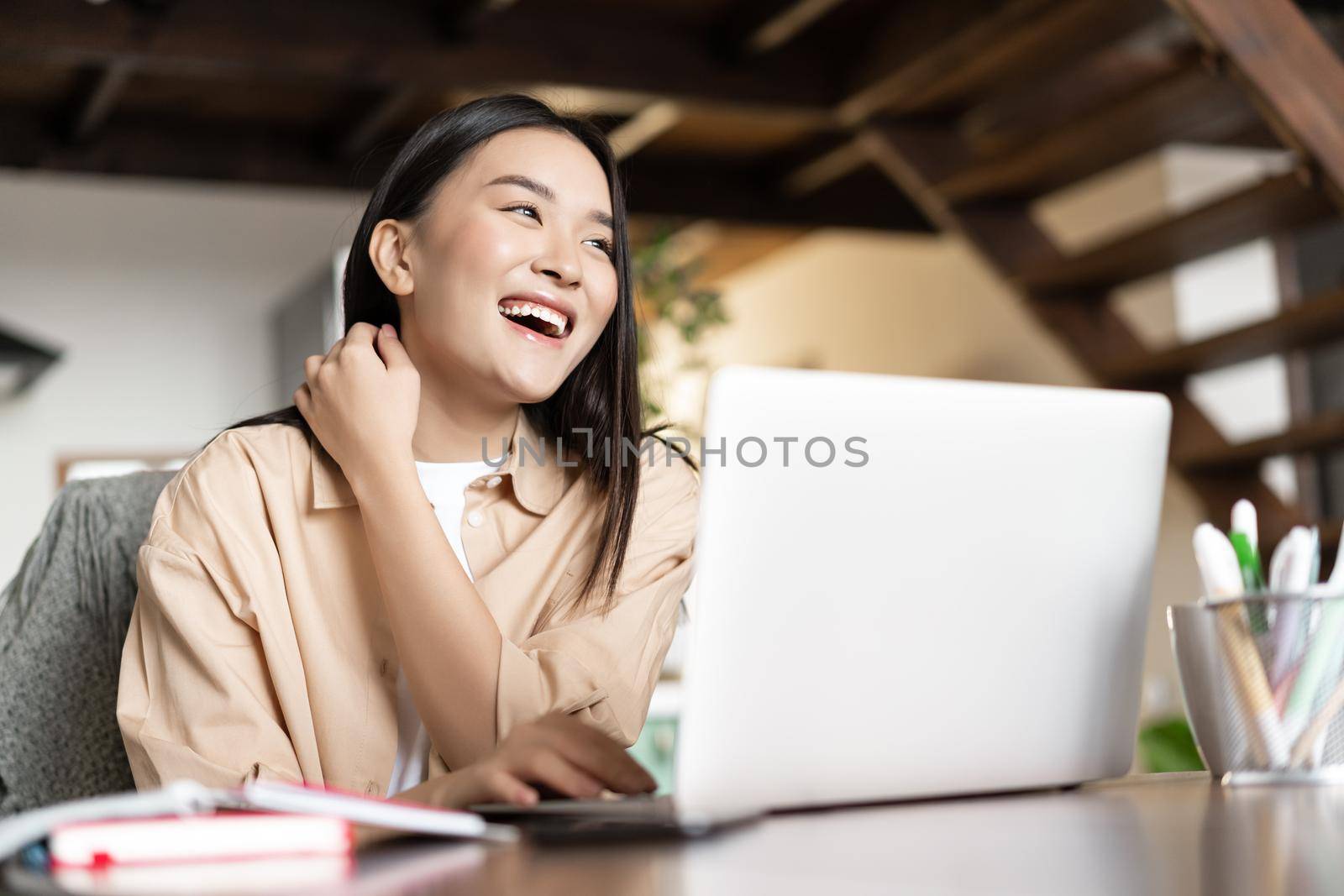 Happy asian woman laughing, working on laptop from home. Girl student studying on computer, online learning, remote education concept.
