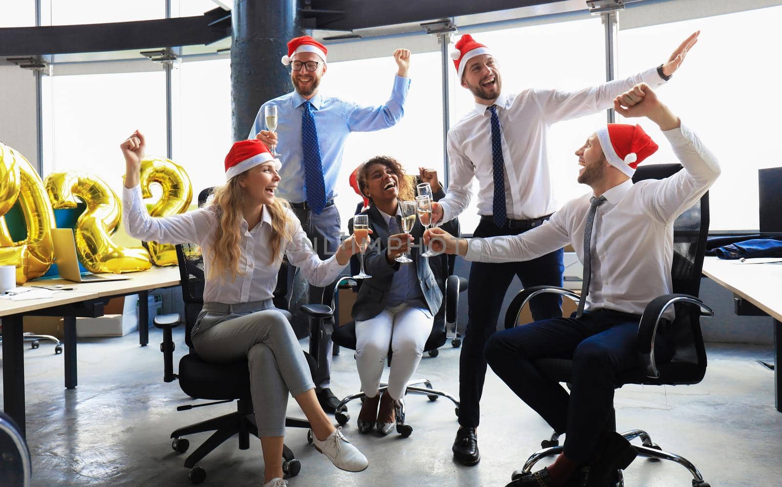 Business people are celebrating holiday in modern office drinking champagne and having fun in coworking. Merry Christmas and Happy New Year 2022