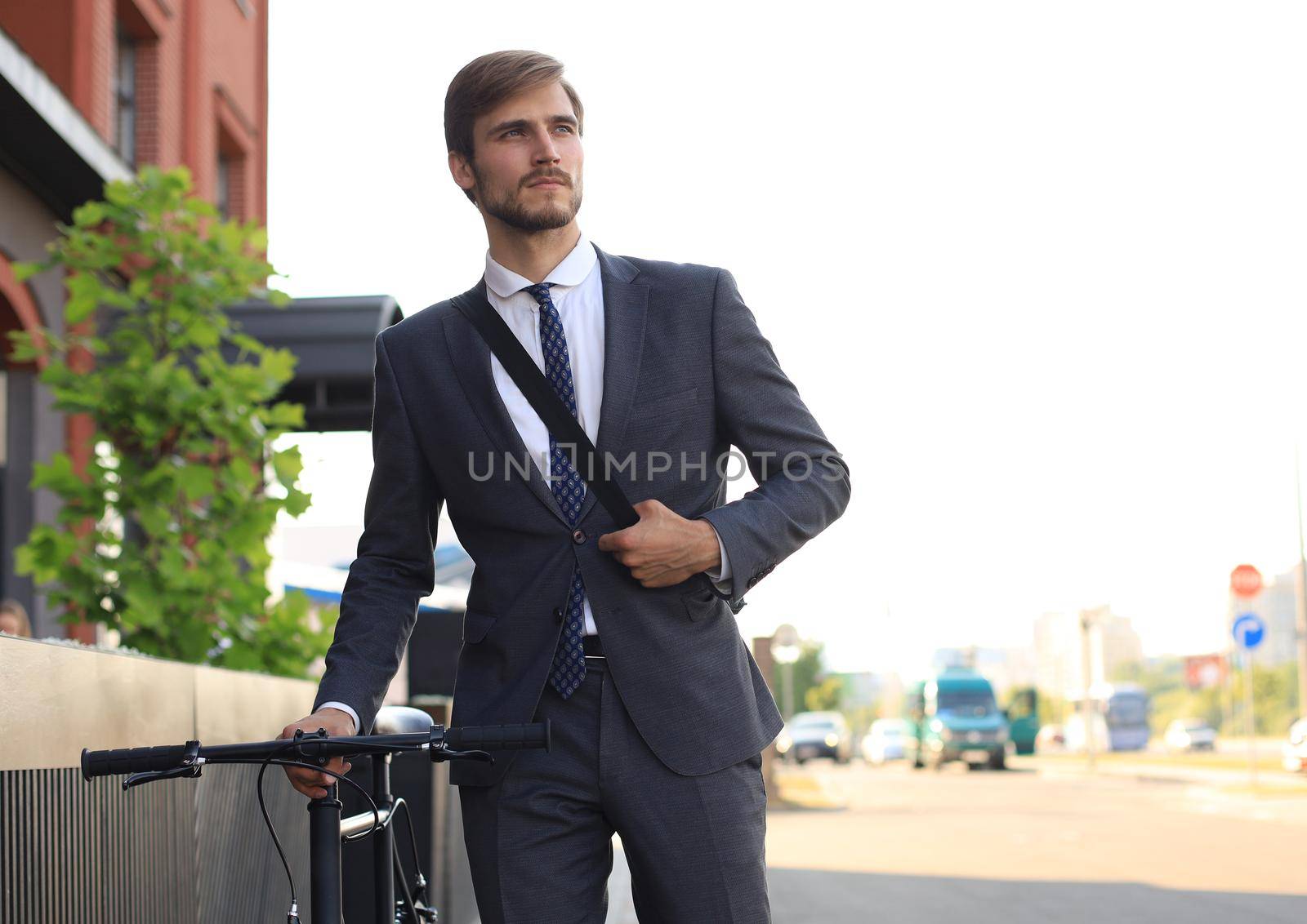 Pensive young businessman walking with bicycle on the street in city