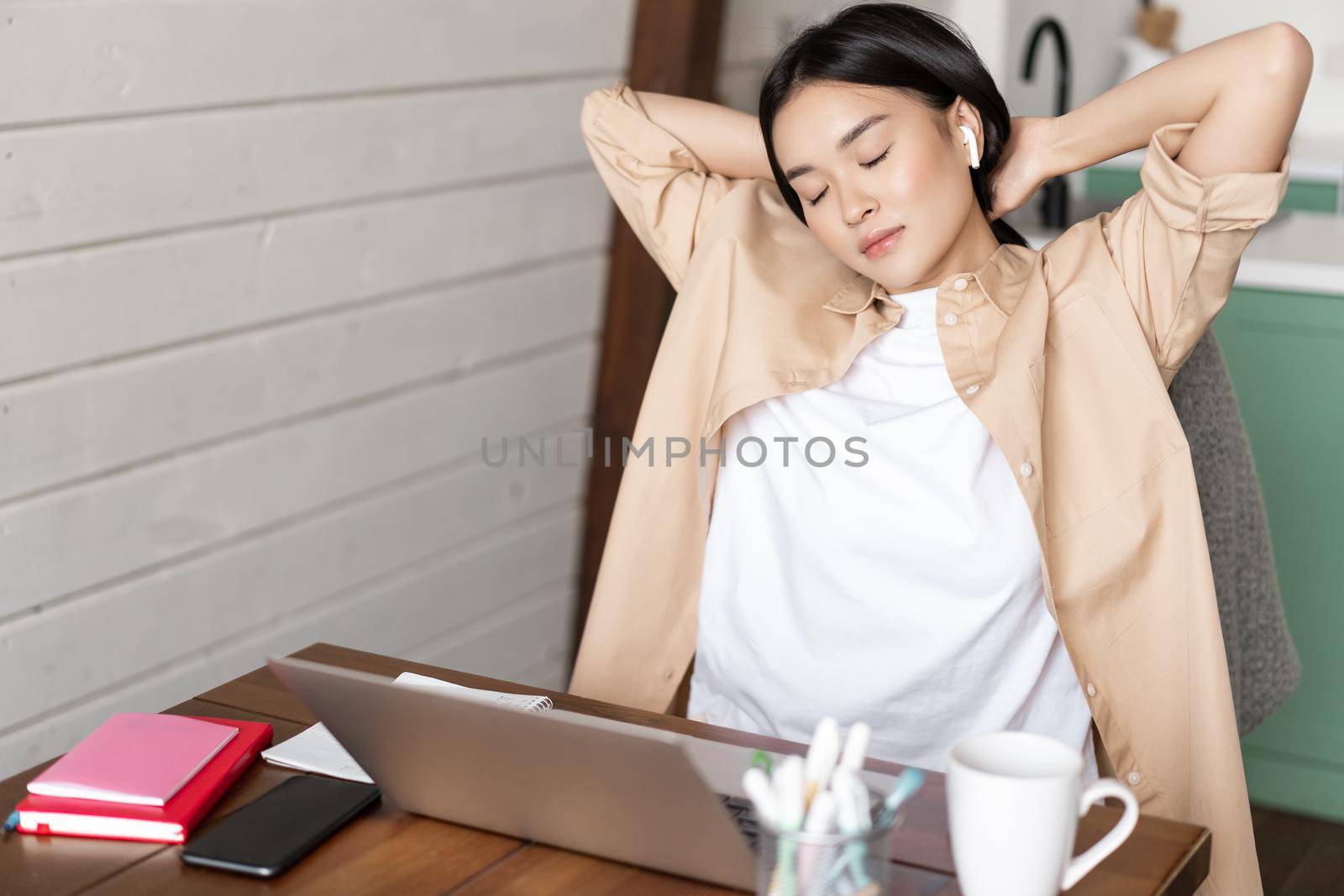 Tired asian girl having break from working, stretching arms after doing homework on laptop, sitting at home, works or studies at home remotely.