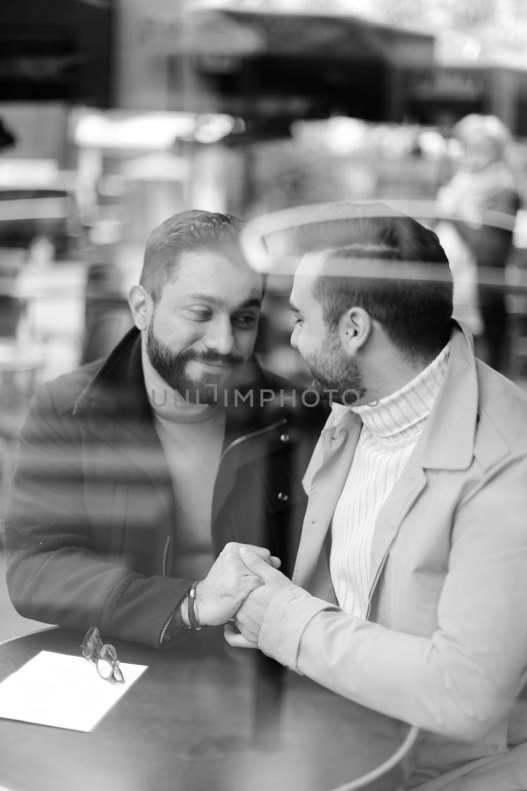 Black and white photo of young gays talking and holding hands, reflection in glass. Concept of same sex couple and lgbt.