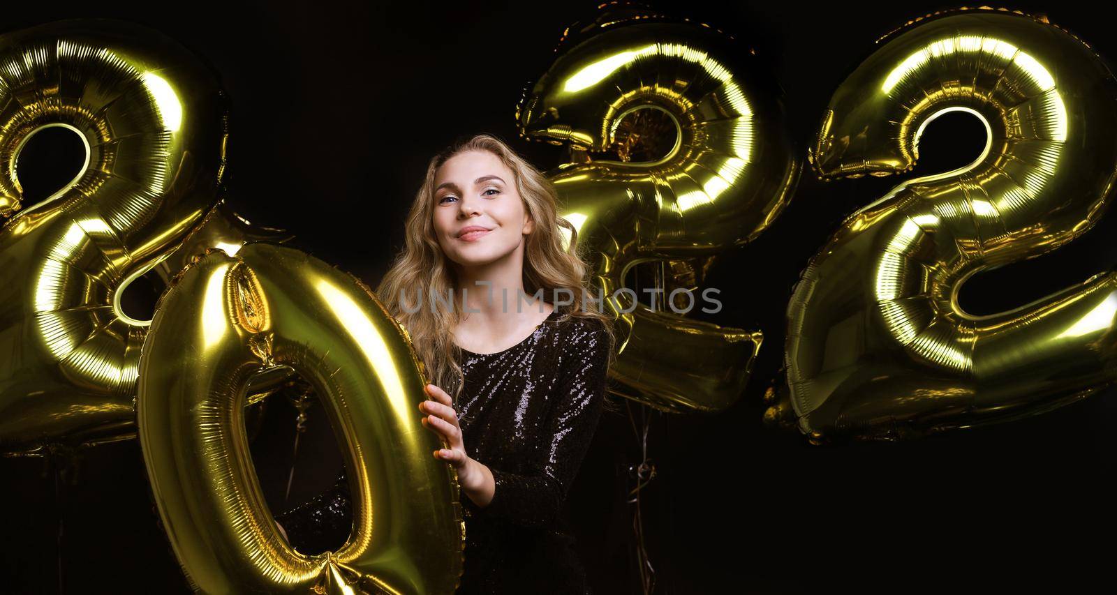Happy gorgeous girl in stylish sexy party dress holding gold 2022 balloons, having fun at Christmas or New Year's Eve Party