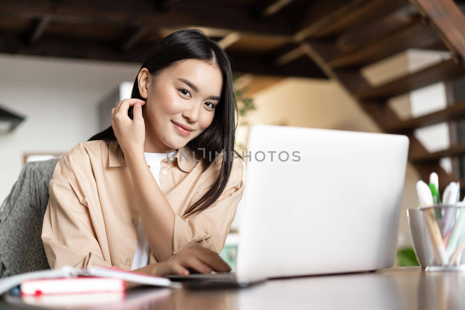 Work from home. Asian girl using laptop computer and smiling, studying at online school.