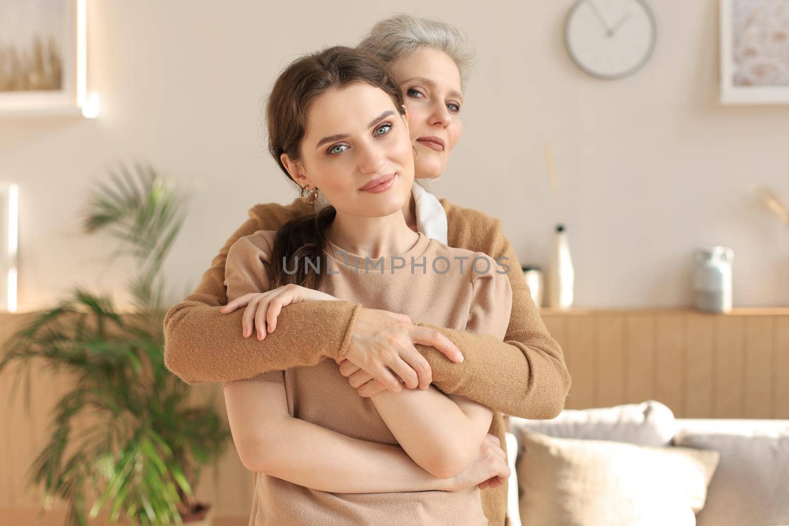 Beautiful mother and daughter. Cheerful young woman is embracing her middle aged mother in living room. Family portrait