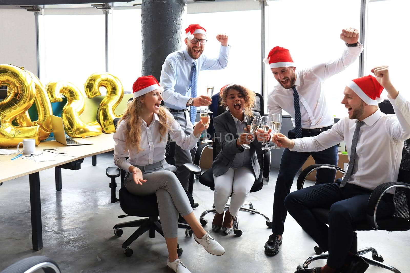 Business people are celebrating holiday in modern office drinking champagne and having fun in coworking. Merry Christmas and Happy New Year 2022