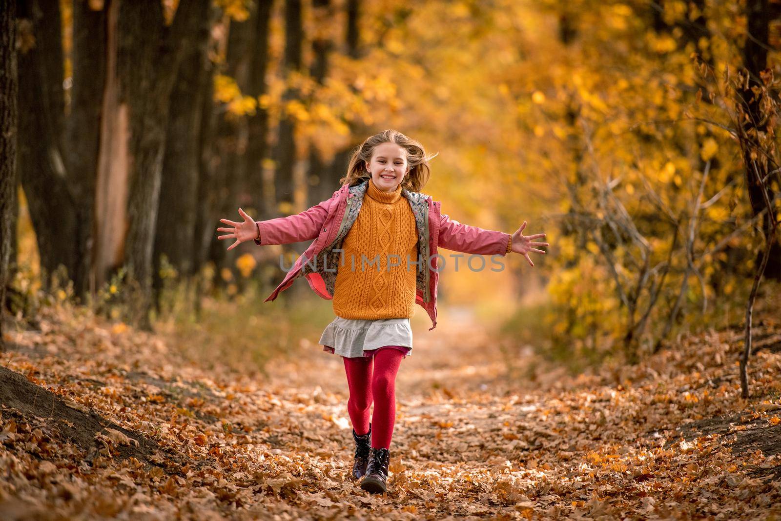 Hsppy girl kid running and jumping at autumn park with yellow trees. Beautiful kid outdoors